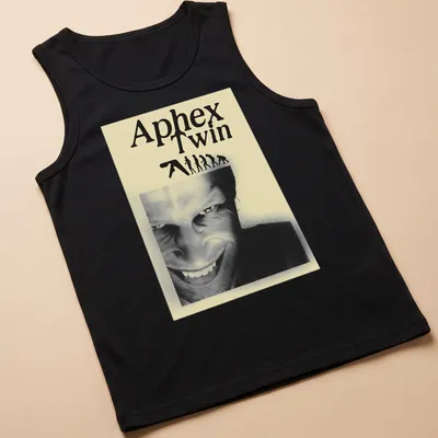 Black and white illustration featuring Aphex Twin text, evolving figures, and a smiling face — printed on a tank top