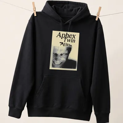 Black and white illustration featuring Aphex Twin text, evolving figures, and a smiling face — printed on a unisex hoodie