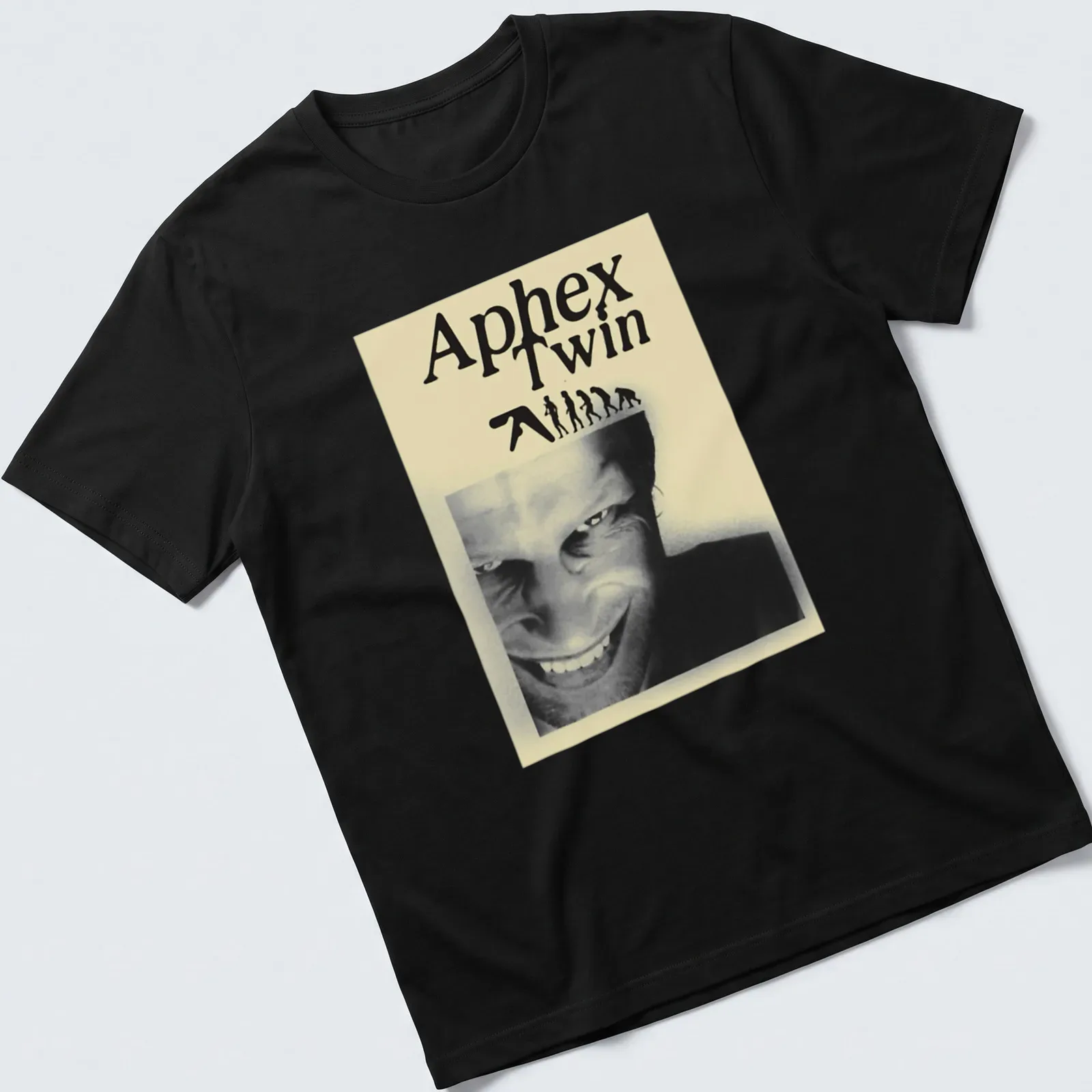 Black and white illustration featuring Aphex Twin text, evolving figures, and a smiling face — printed on a unisex t-shirt
