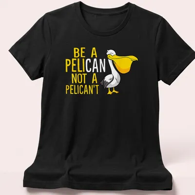 Cartoon pelican graphic with humorous text 'Be A Pelican Not A Pelican't' in yellow, white, and black — printed on a women's shirt