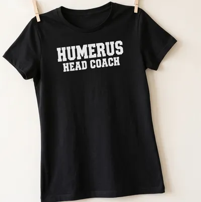 White T-shirt with bold text 'HUMERUS HEAD COACH' and anatomical humerus bone graphic — printed on a women's shirt
