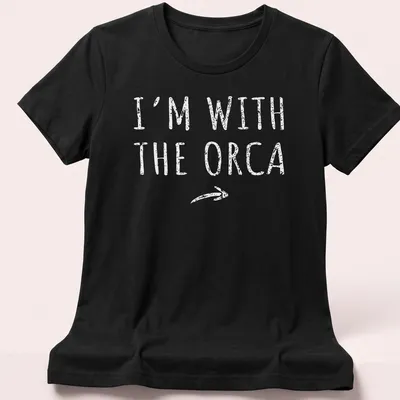 Playful orca-themed shirt with bold text 'I'm With The Orca' for Halloween — printed on a women's shirt