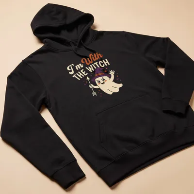 Playful cartoon ghost with witch hat and text 'I'm With THE WITCH' in Halloween colors — printed on a unisex hoodie