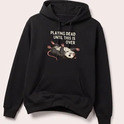 Cartoon opossum with silly expression and text about playing dead during tough times — printed on a unisex hoodie