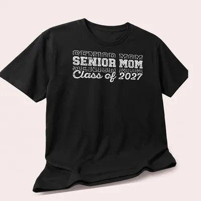 Bold text Senior Mom Class of 2027 graduation t-shirt in white — printed on a unisex t-shirt (angled view)