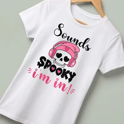 Cartoon skull with headphones and text 'Sounds Spooky I'm in!' in pink, black, and white — printed on a women's shirt