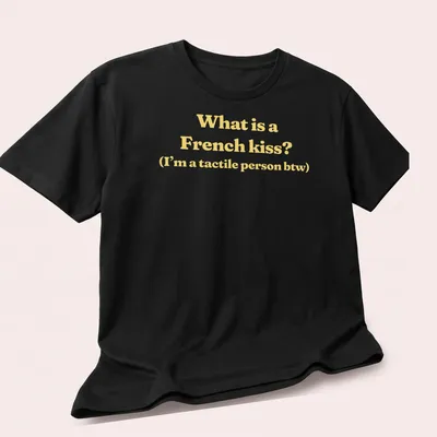 Text print reading What is a French kiss? I’m a tactile person btw in yellow and white — printed on a unisex t-shirt (angled view)